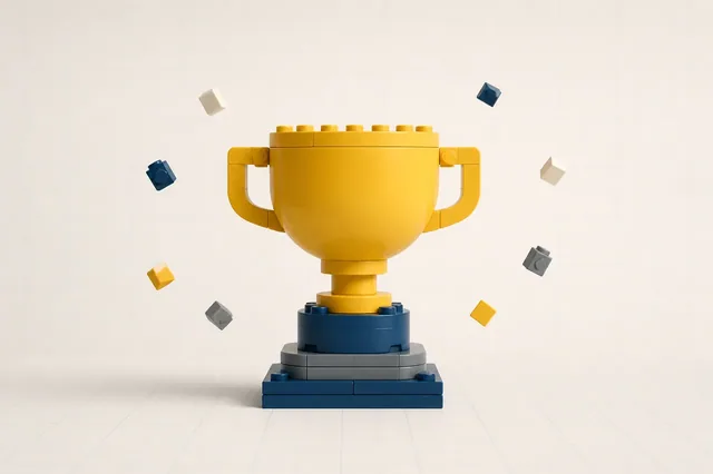 A golden trophy cup built entirely from toy bricks on a stepped base, with small bricks floating like confetti around it.